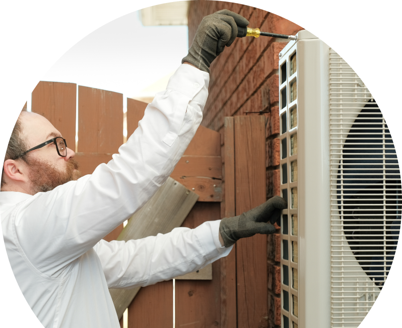 Shines service personnel working on an AC condenser, using a screwdriver to secure the unit's panel outdoors beside a wooden fence.