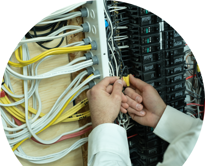 Shines service personnel working on electrical installations, connecting wires inside a residential breaker panel with neatly arranged colored cables on a plywood backing. Shines service personnel working on electrical installations, connecting wires inside a residential breaker panel with neatly arranged colored cables on a plywood backing.