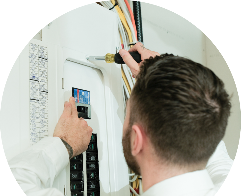 Shines electrician using a screwdriver to perform an electrical panel upgrade, working near organized wiring in a residential wall. Shines electrician using a screwdriver to perform an electrical panel upgrade, working near organized wiring in a residential wall.