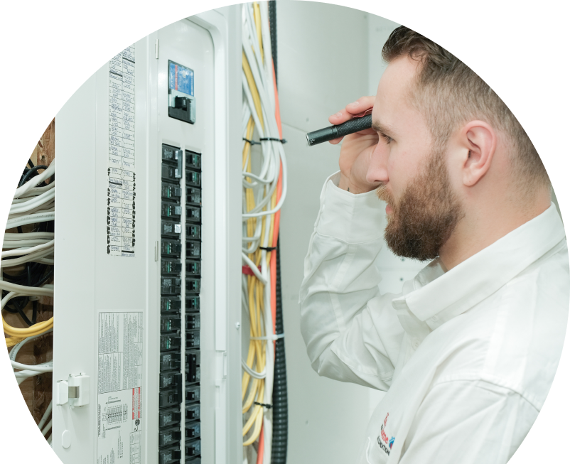 Shines electrician inspecting residential electrical panel wiring with a flashlight, checking connections and circuit labels.