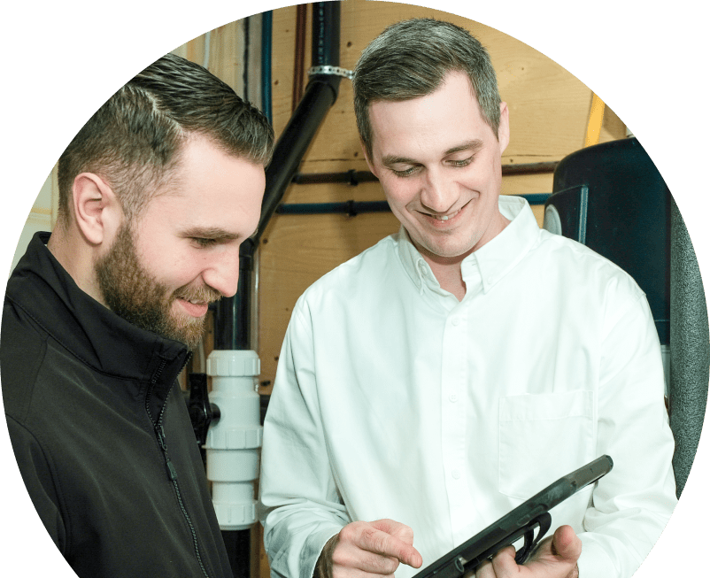 Shines specialist reviewing maintenance plan options with a smiling homeowner using a tablet, inside a utility room with visible piping.