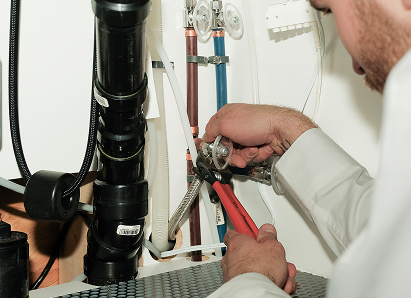 Using two pipe wrenches, a Shines professional plumber services a pipe connection near a vertical flue or vent pipe. Using two pipe wrenches, a Shines professional plumber services a pipe connection near a vertical flue or vent pipe.